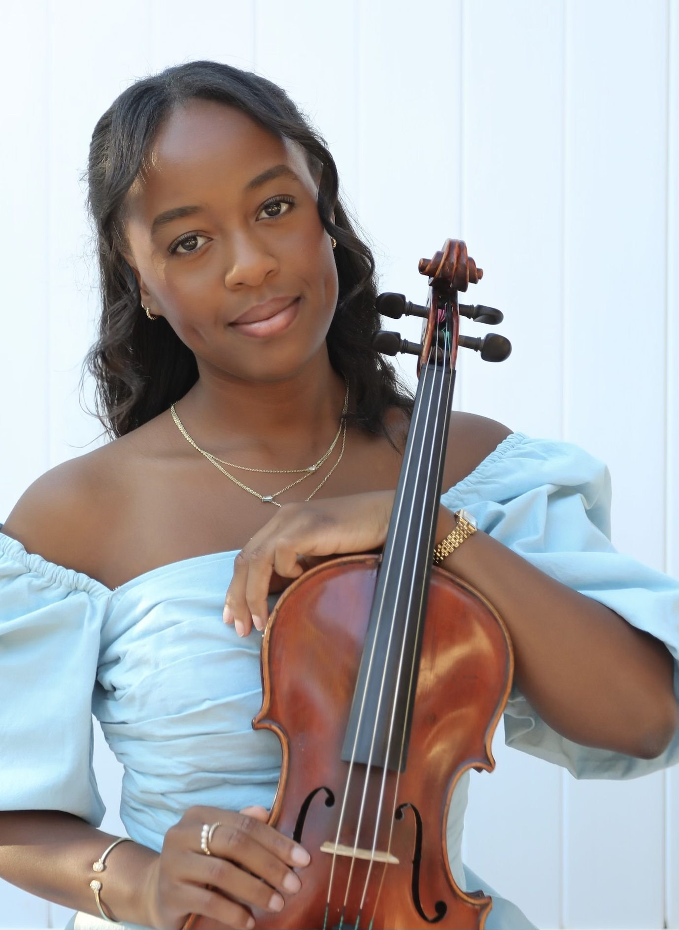 Young woman holding a violin and smiling gently.