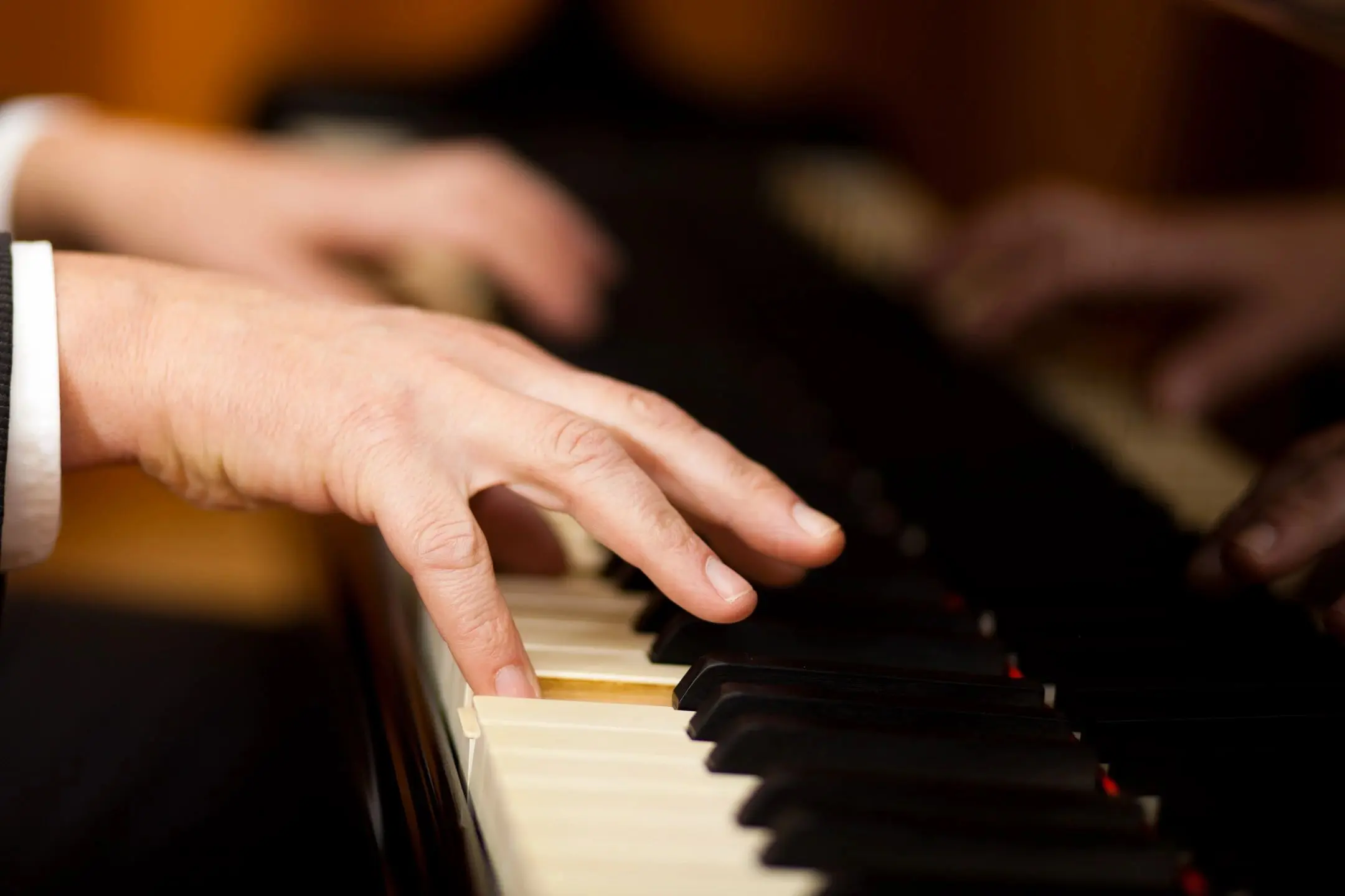 Close-up of hands playing piano keys with warm lighting.