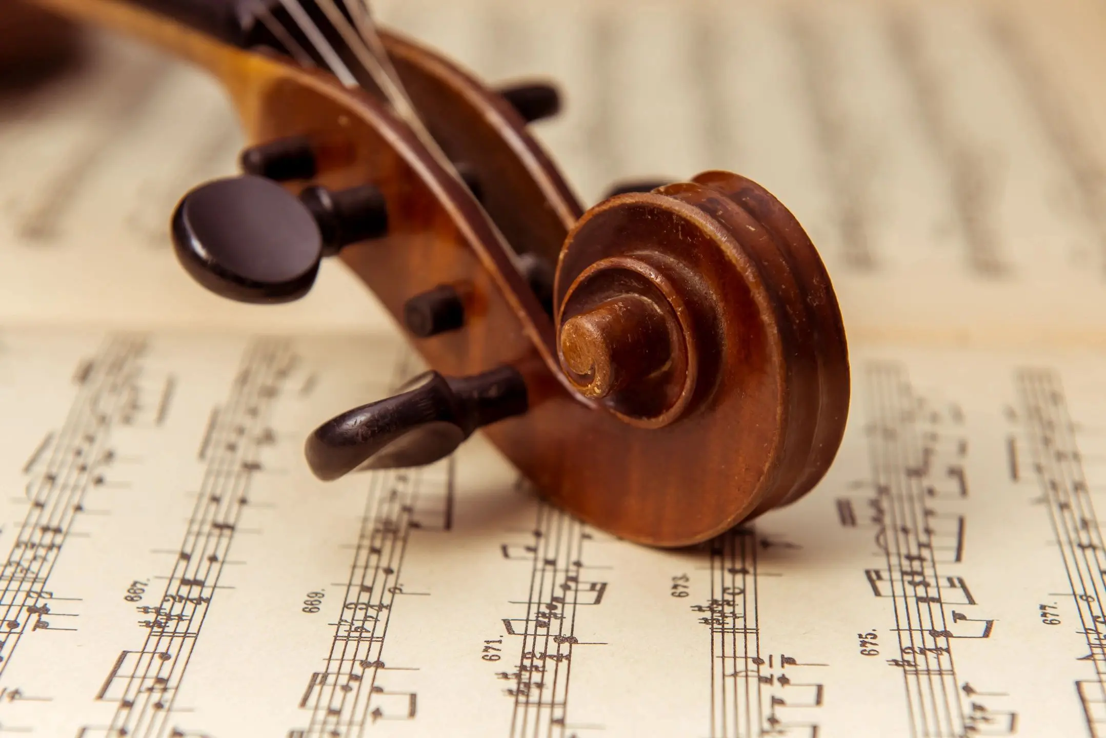 Close-up of a violin scroll resting on sheet music.